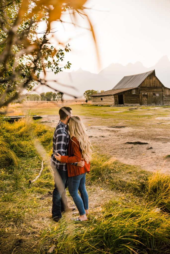 Grand teton engagment couple standing looking at mormon row barn
