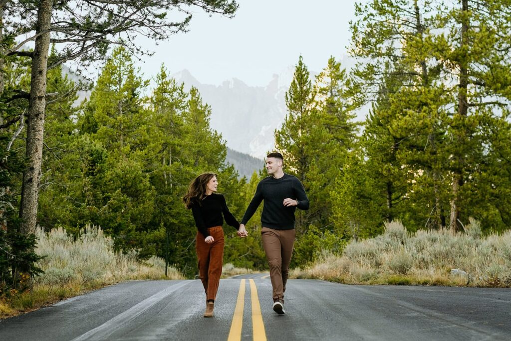 Couple running down national park road with Tetons in background