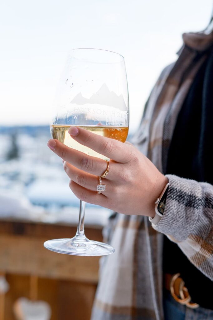 A Jackson Hole winery glass of crafted wine and a woman's hands with a beautiful diamond ring on her finger. 