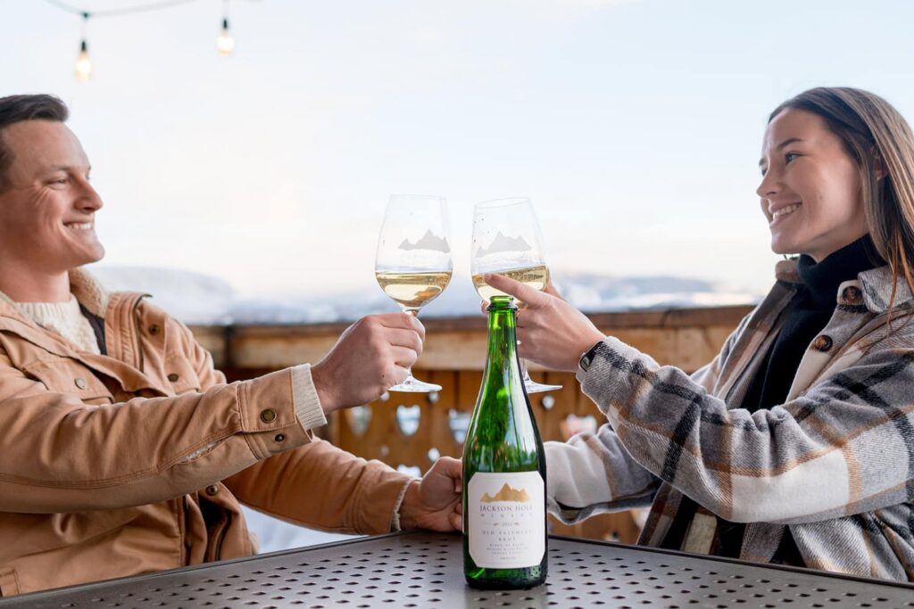 A couple is sharing glasses of wine and a cheers in front of the clock tower at Jackson hole mountain resort