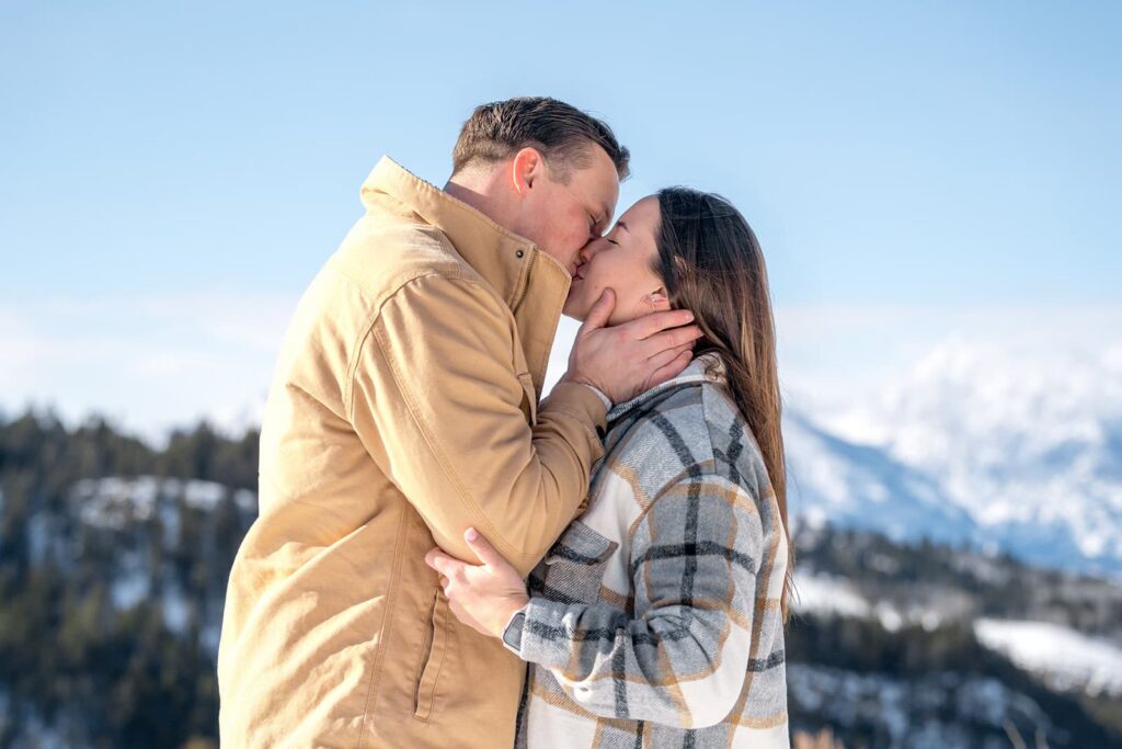 A man and woman share a kiss with the grand tetons behind them