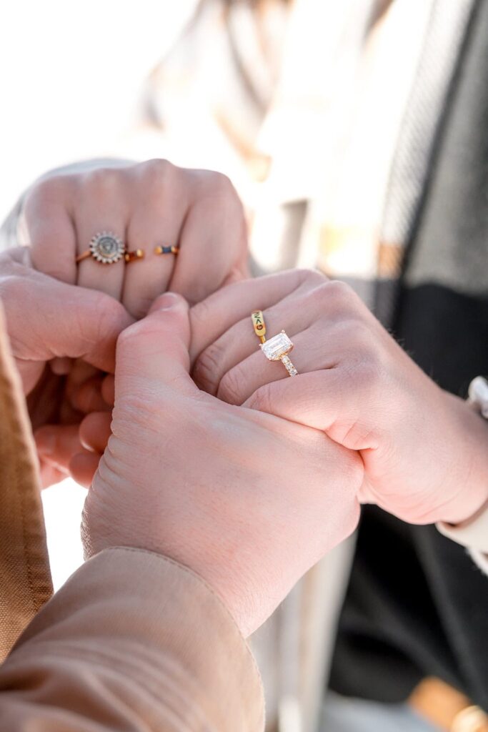 A couple hold hands and show off a beautiful diamond engagement ring