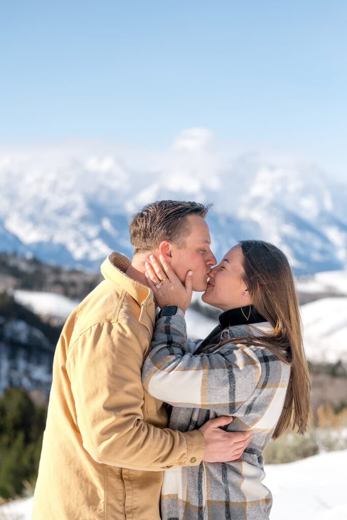A man kisses a woman on the nose as she shows off her wedding ring in front of the grand teton mountains in the winter captured by Karina Dopp - A jackson hole wedding photographer
