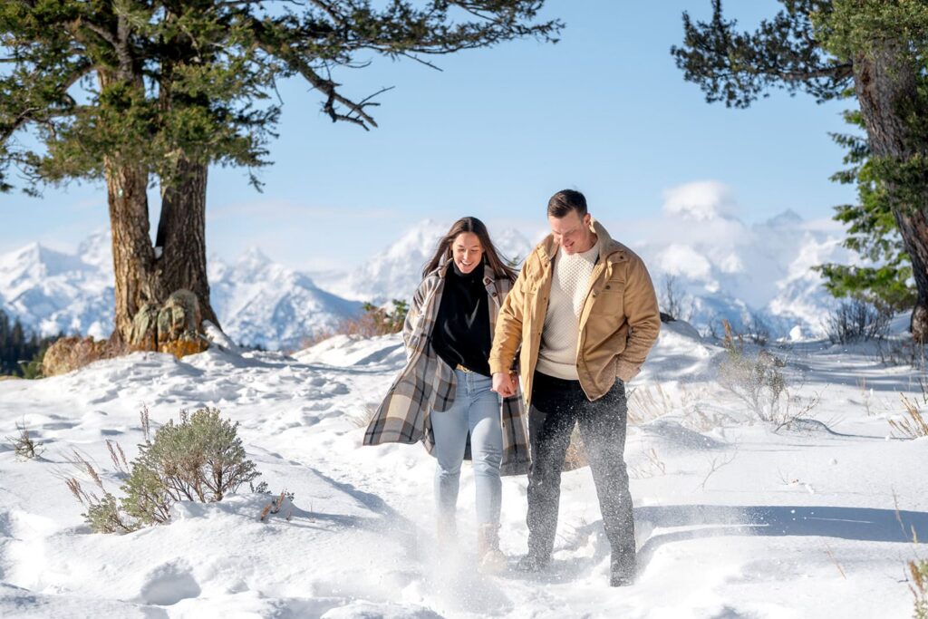 A couple kick snow at the camera as they walk from the Wedding tree in grand teton national park 