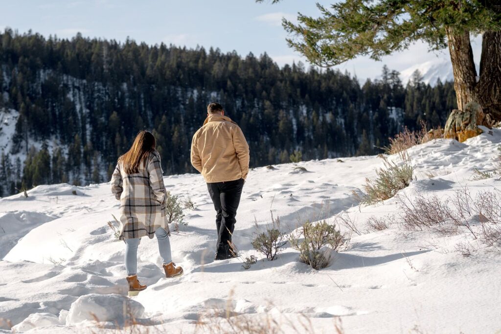 A man and woman are walking in the snow on a trail to the Wedding tree in Grand Teton National Park 