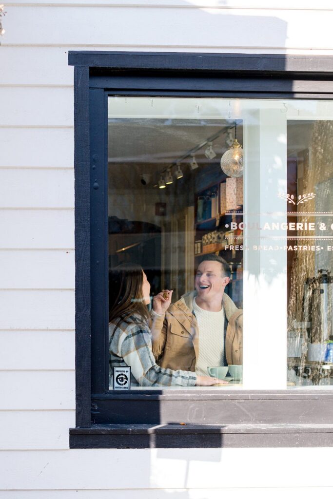 A man shares a bite of his food with a woman as seen from a window at Persephonie's bakery in Jackson,  Wyoming