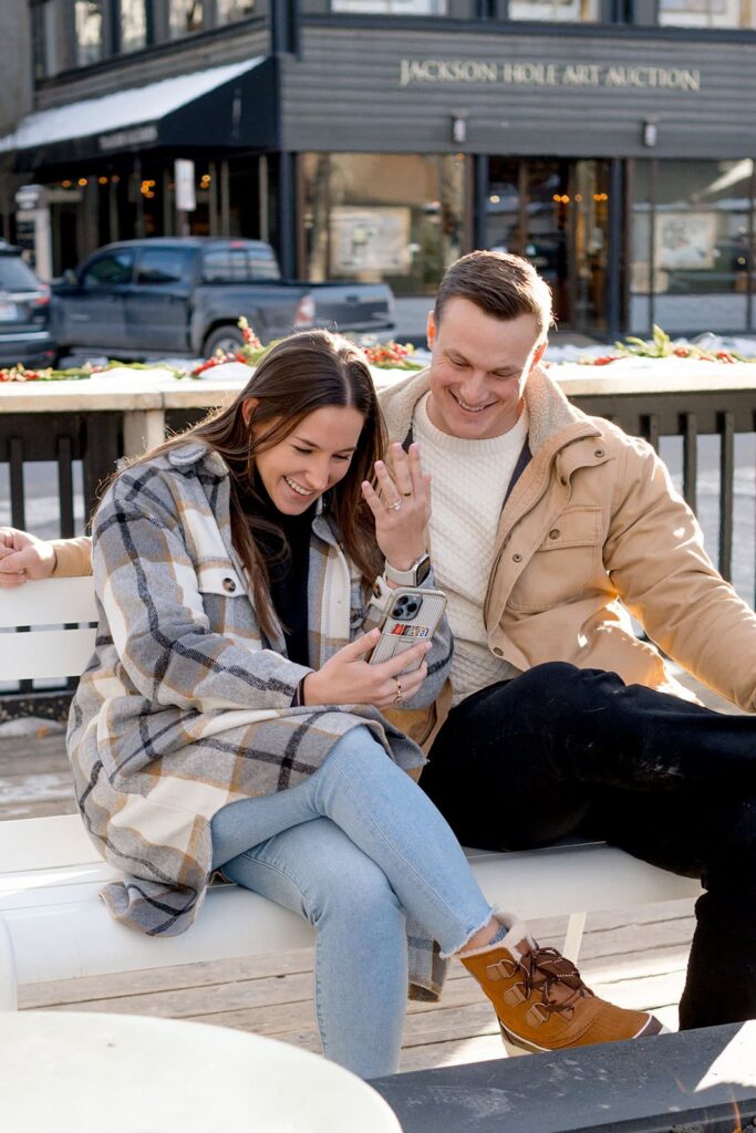 A couple shows off an engagement ring to someone on facetime in Jackson hole town square 