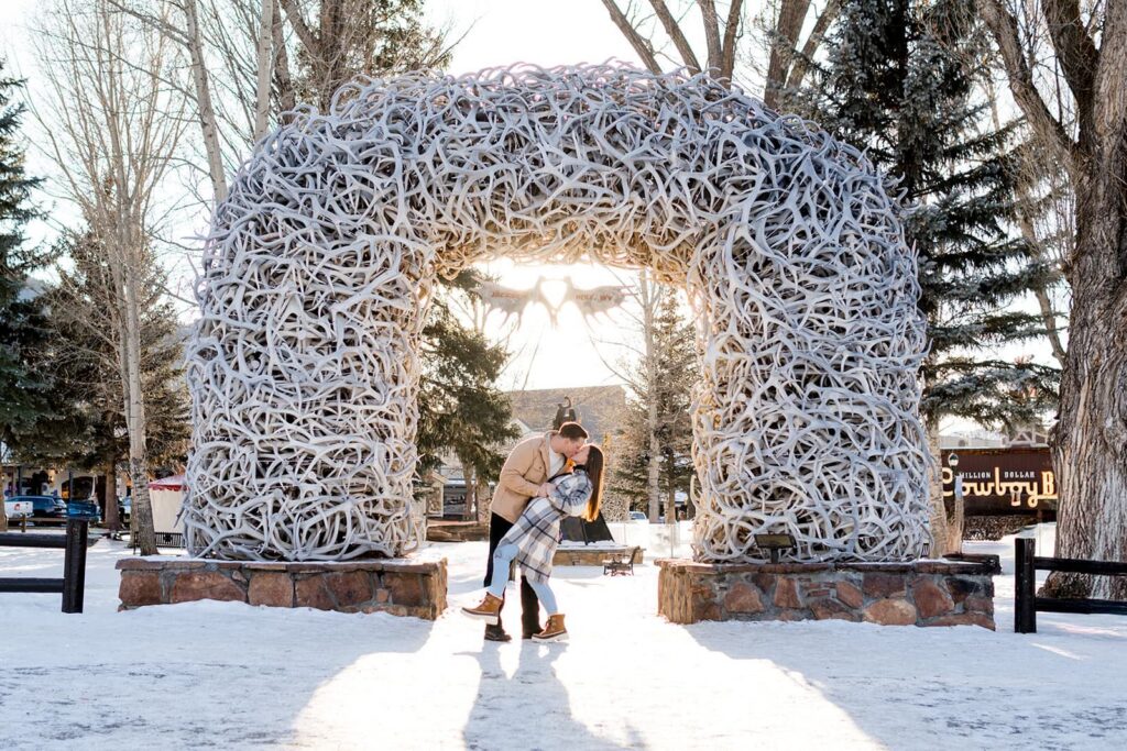 A couple shares a kiss in front of the iconic antler arches in Jackson hole town square 