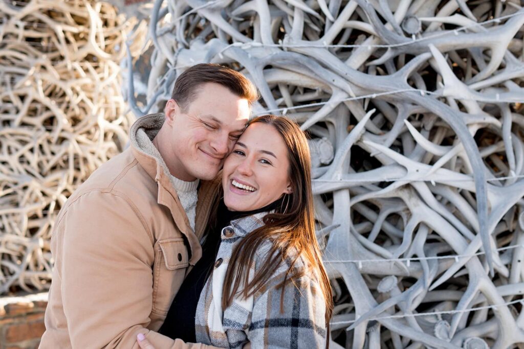 A couple is hugging in front of jackson hole's antler arches. 